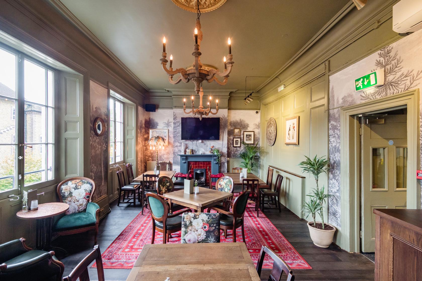 A lounge with vintage armchairs, patterned rugs, potted plants, and a chandelier at Island Queen.