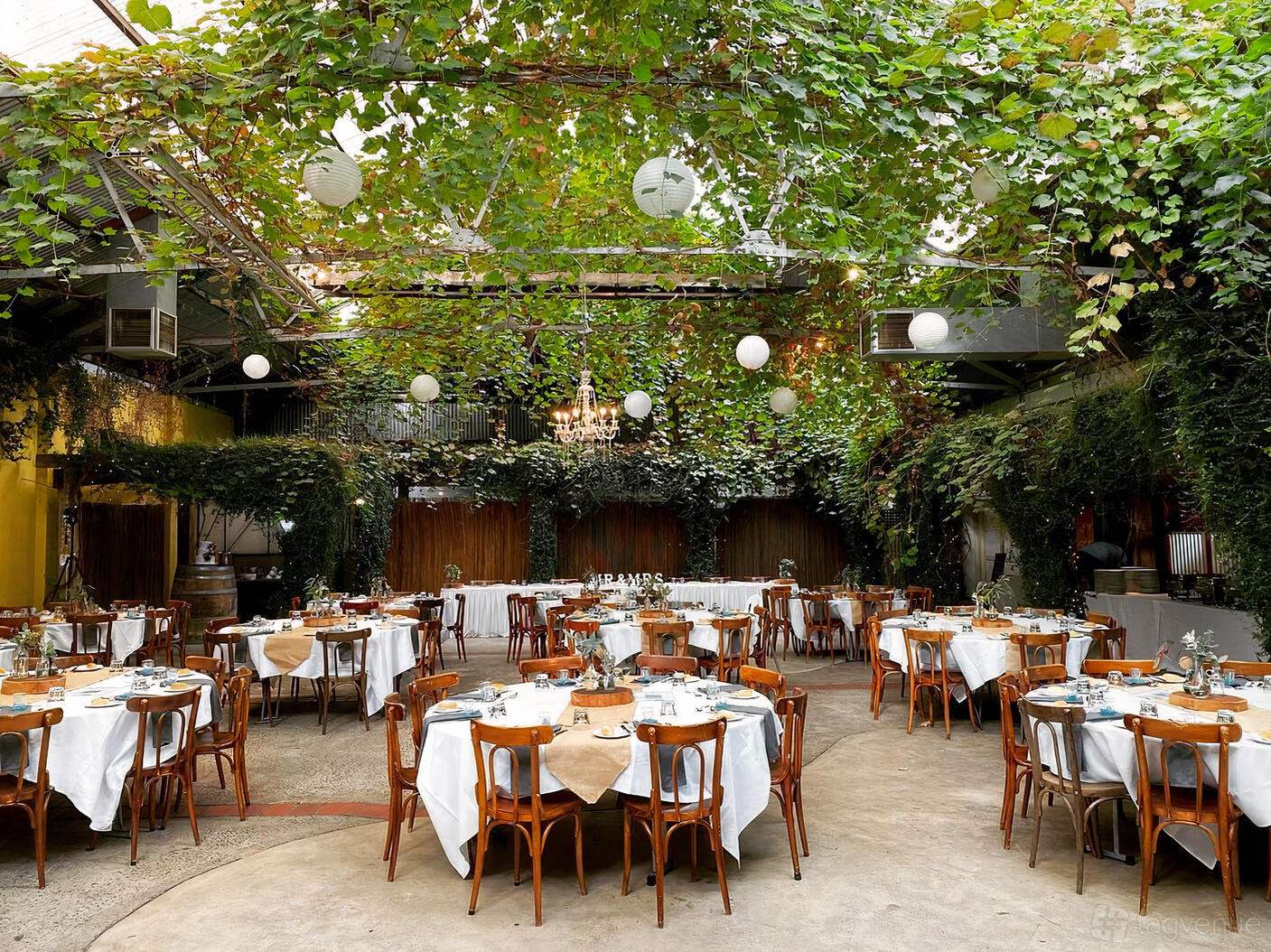 An event venue with hanging greenery, round tables draped in white linens, and globe pendant lights at Radcliffes.