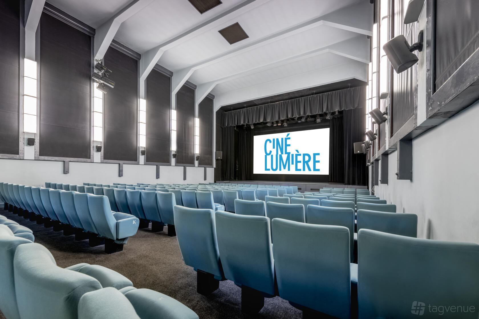 A screening room with teal theater seats, tall windows, and a large projection screen at Institut français au Royaume-Uni.