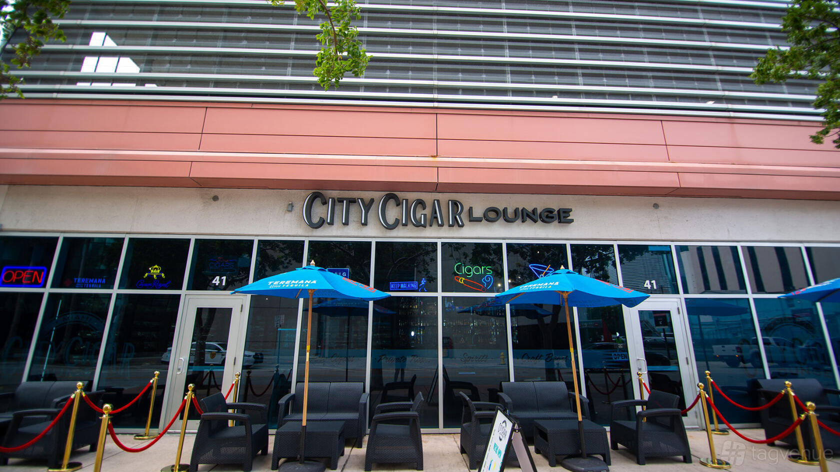 A pub with outdoor seating, blue umbrellas, and black lounge chairs at City Cigar Lounge.