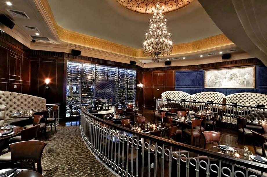 A restaurant with tufted banquettes, a grand chandelier, and a glass wine display at Empire Steak House East.