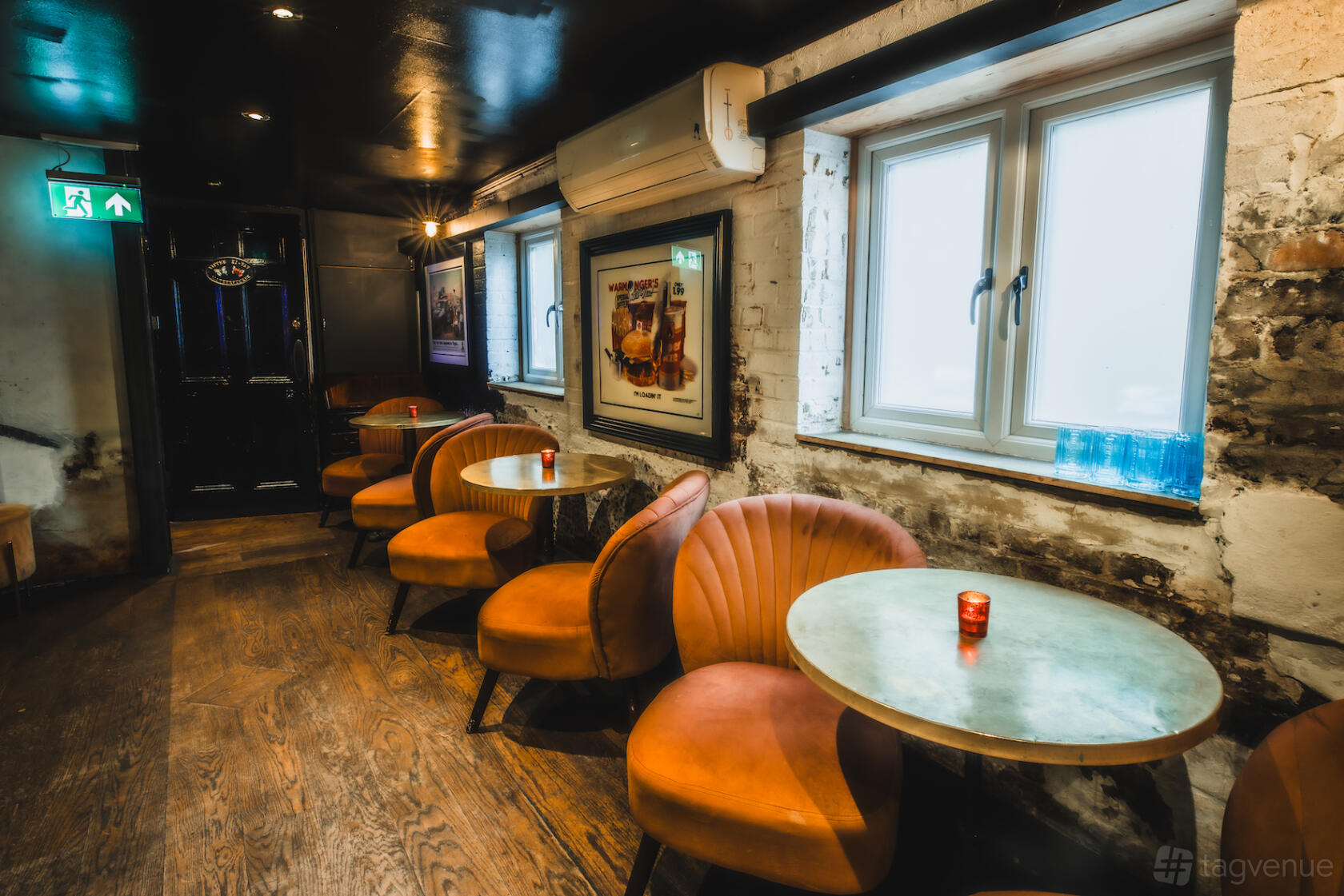 A function room with round tables, orange velvet chairs, and exposed brick walls at Callooh Callay Shoreditch.