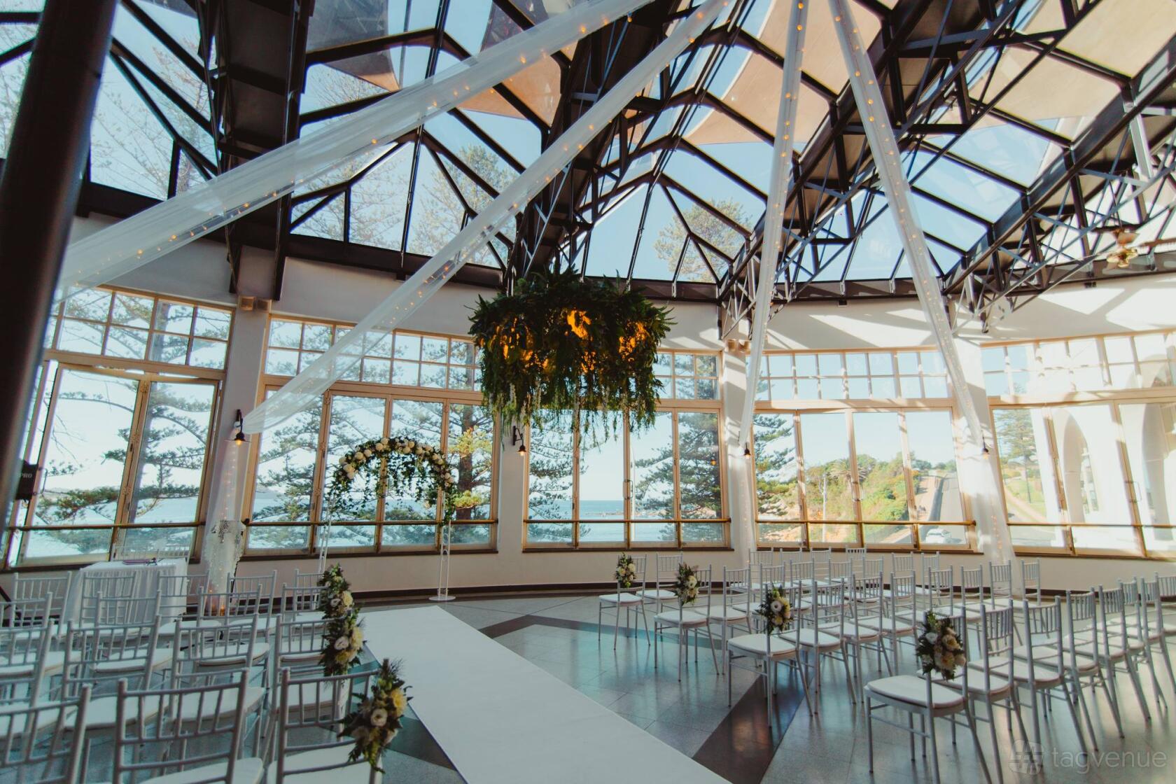 An event space with floor-to-ceiling windows, draped ceiling lights, and greenery at Crowne Plaza Terrigal Pacific