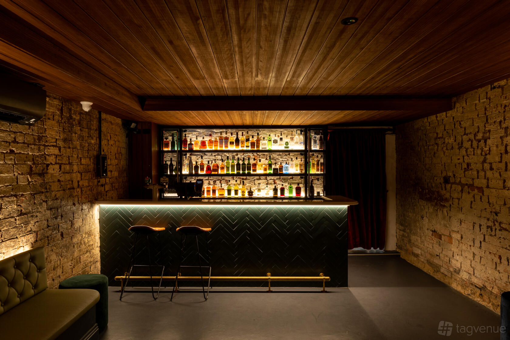 A function room in a bar with exposed brick walls, wood ceiling, and a backlit bar at Maeve Fox.