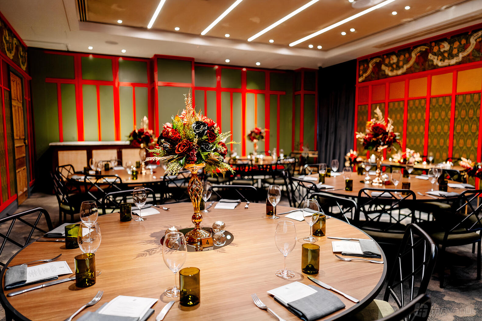 A hotel function room with round tables, elaborate floral centerpieces, and red-accented panel walls at Ovolo The Valley.