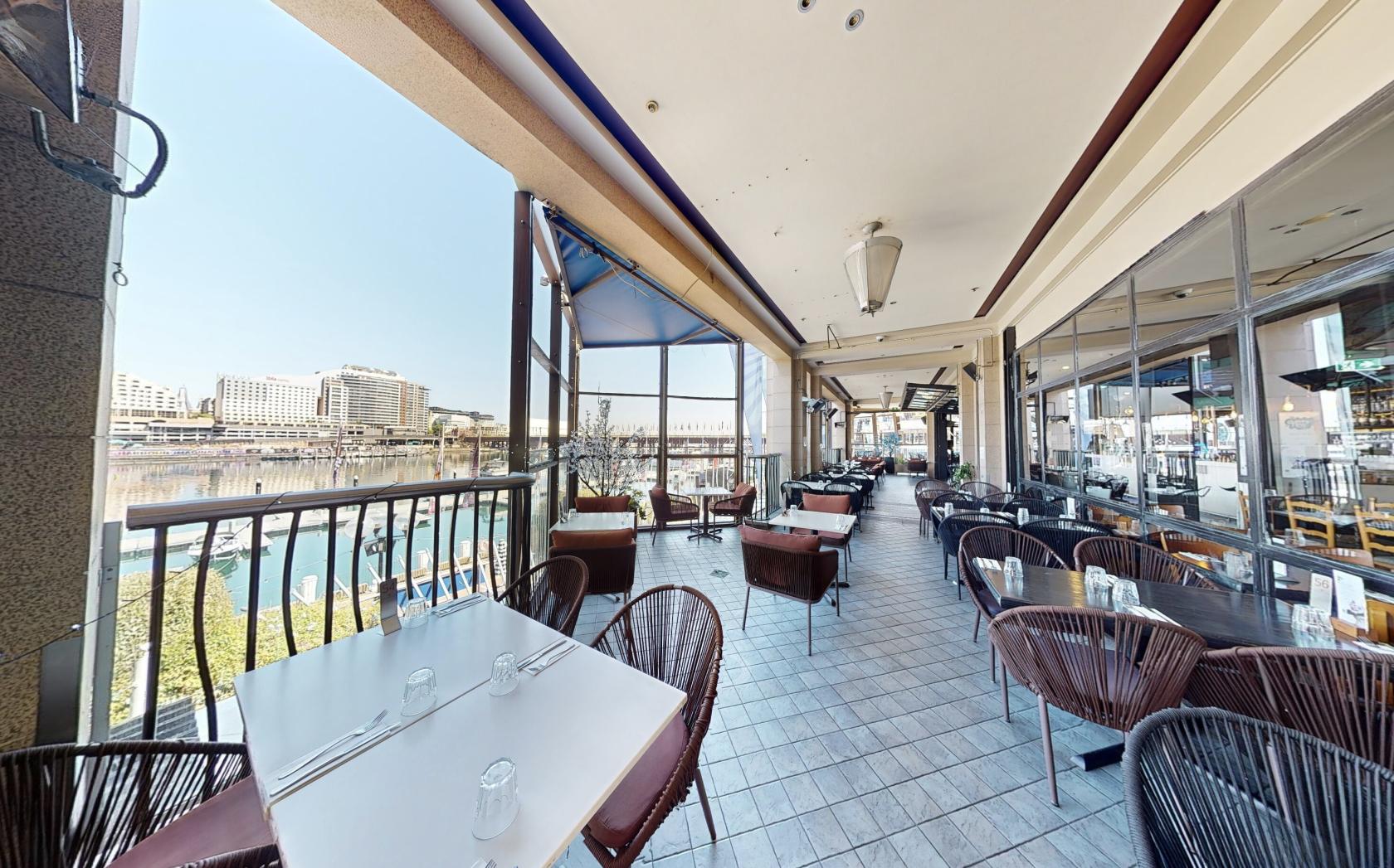 An outdoor dining area with tiled floors, glass railings, and wicker chairs overlooking the water at Blackbird Cafe.
