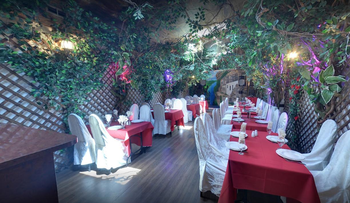 A restaurant with long tables draped in red tablecloths, white chair covers, and greenery overhead at Moldova Restaurant.