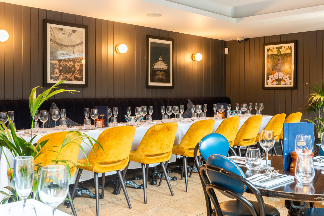 A dining room with yellow velvet chairs, long white-clothed tables, and framed wall art at Browns Glasgow.