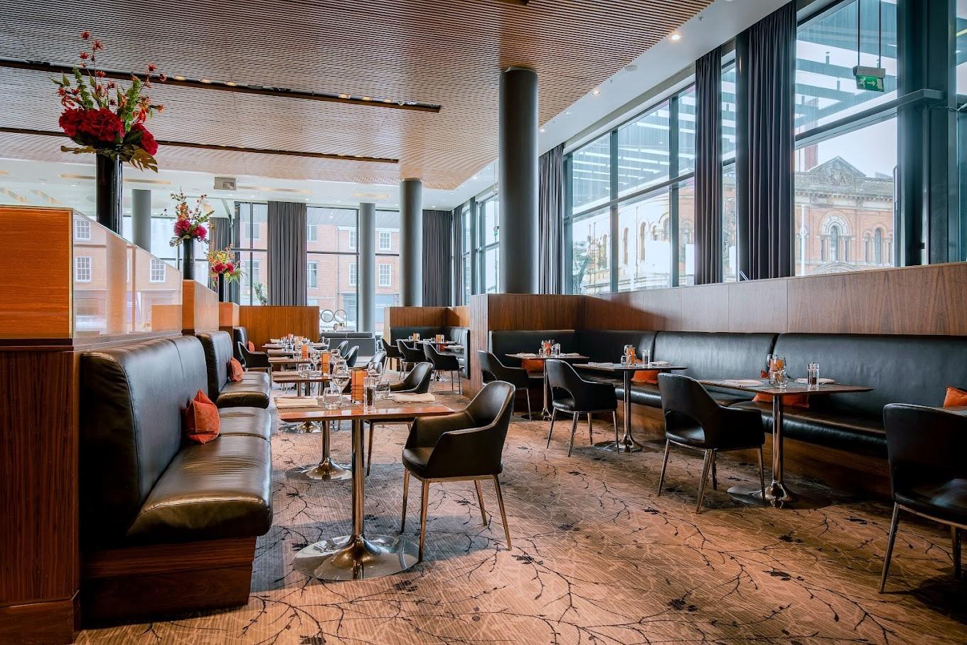 An event space in a restaurant with floor-to-ceiling windows, black leather seating, and round tables at Podium.