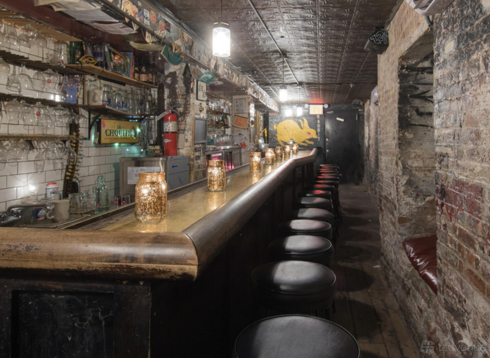 An intimate bar event space with exposed brick walls, a long wooden bar, and candlelit jars at 124 Rabbit Club.