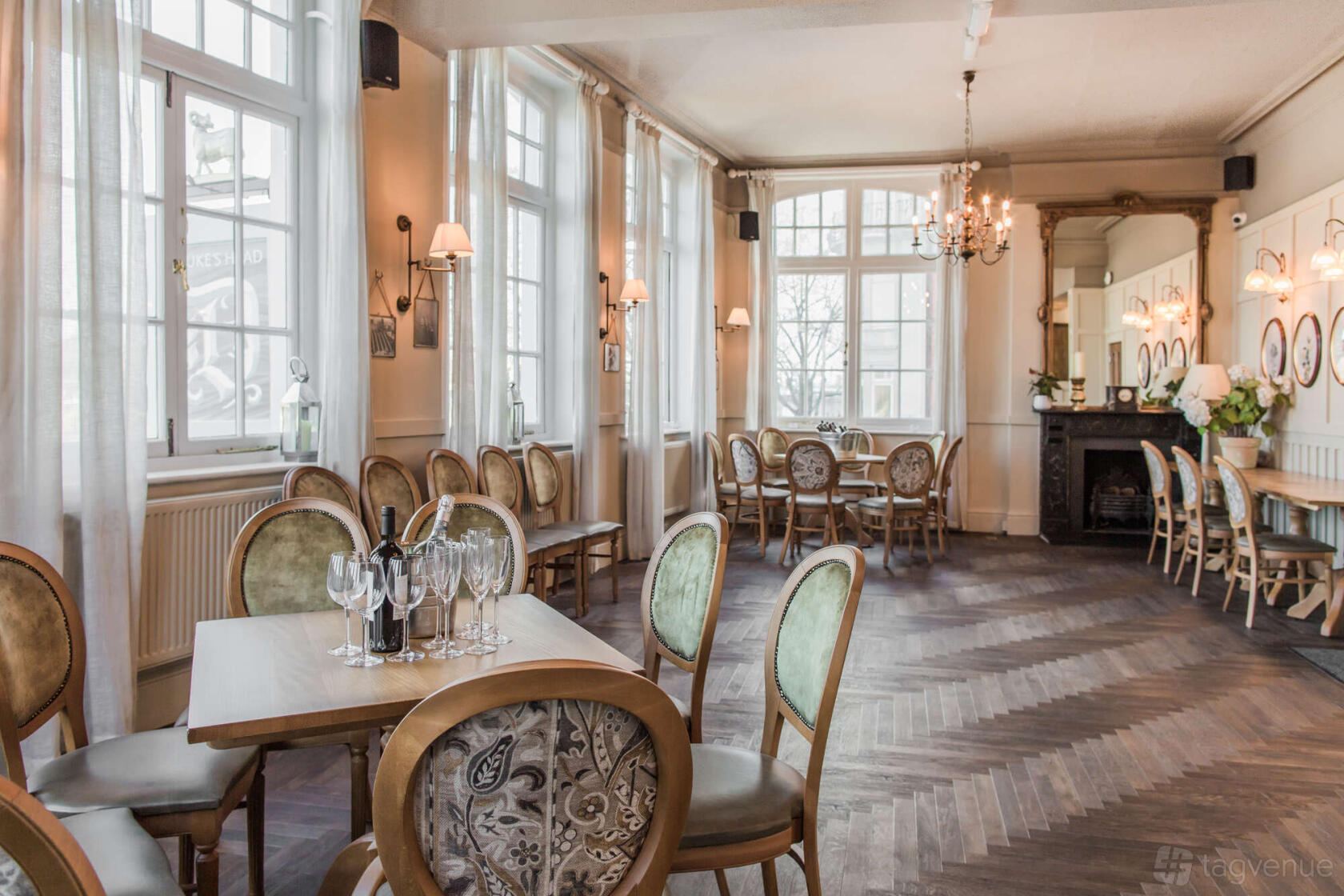 A function room in a pub with large windows, parquet flooring, chandeliers, and vintage chairs at Duke's Head Putney.