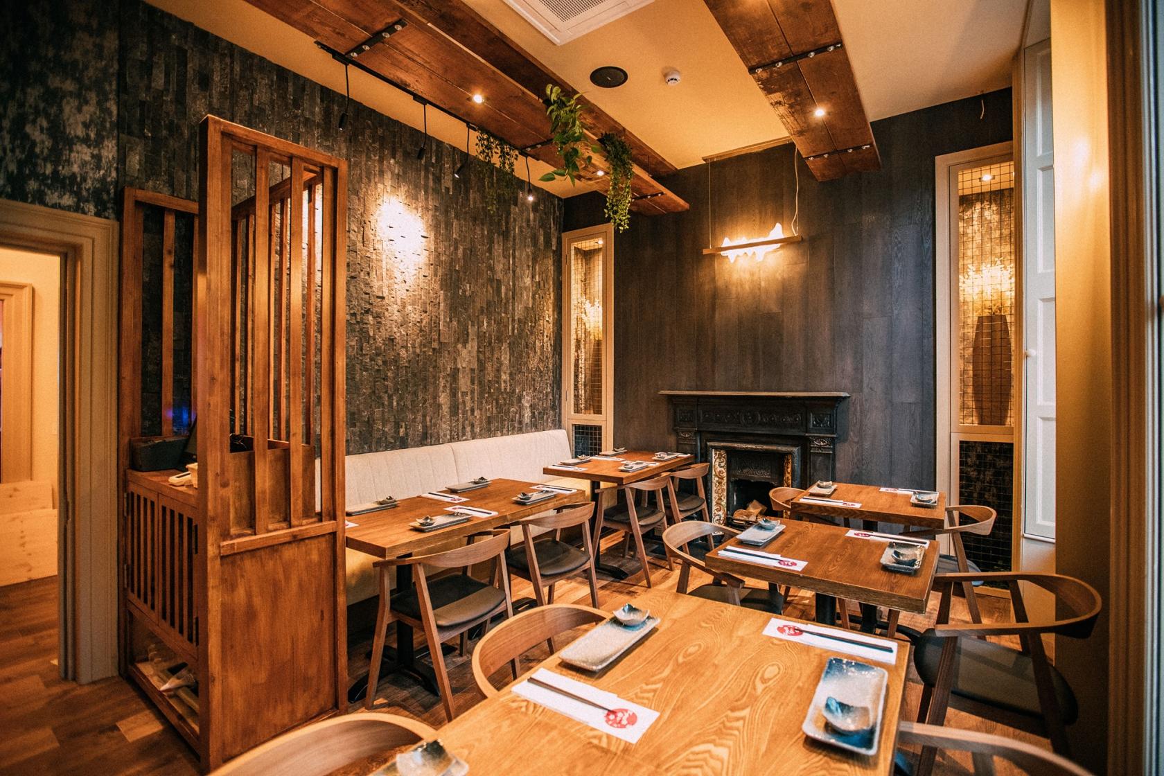 A dining room with wooden tables, textured dark walls, and a decorative fireplace at Maneki Japanese Cuisine & Karaoke Box.
