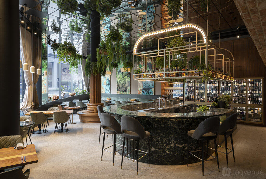 A restaurant with a curved marble bar, hanging greenery, and floor-to-ceiling windows at Omnia Bistro & Bar.