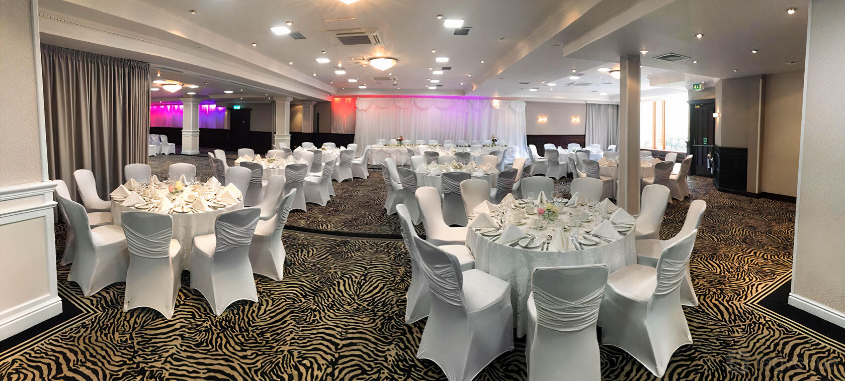 An event space with round tables covered in white linens and zebra-print carpet at The Glynhill Hotel.