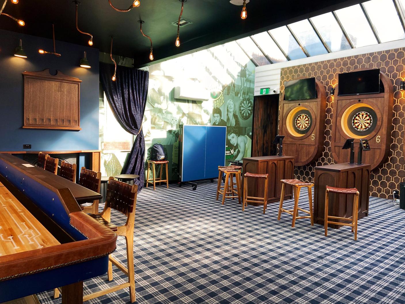 An event space in a bar with dartboards, plaid carpet, bar seating, and natural skylight at Ballers Clubhouse Carlton.