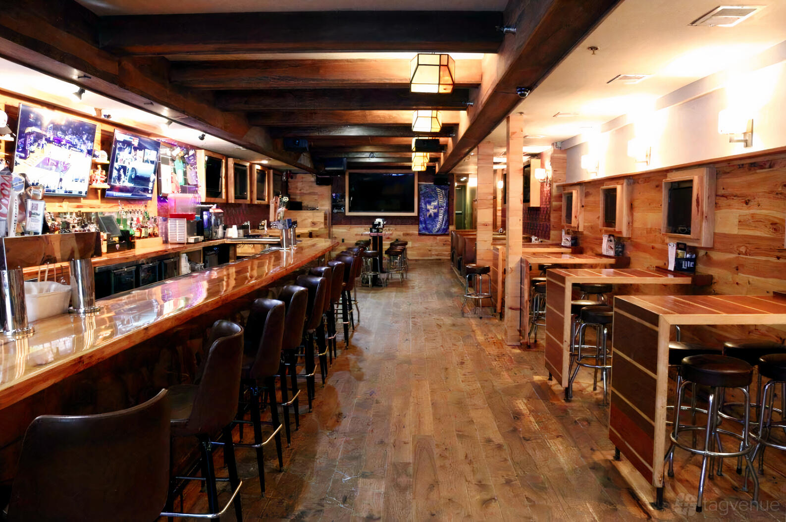 A dining room in a bar with wood-paneled walls, a long polished bar, and high-top tables at The Pony.
