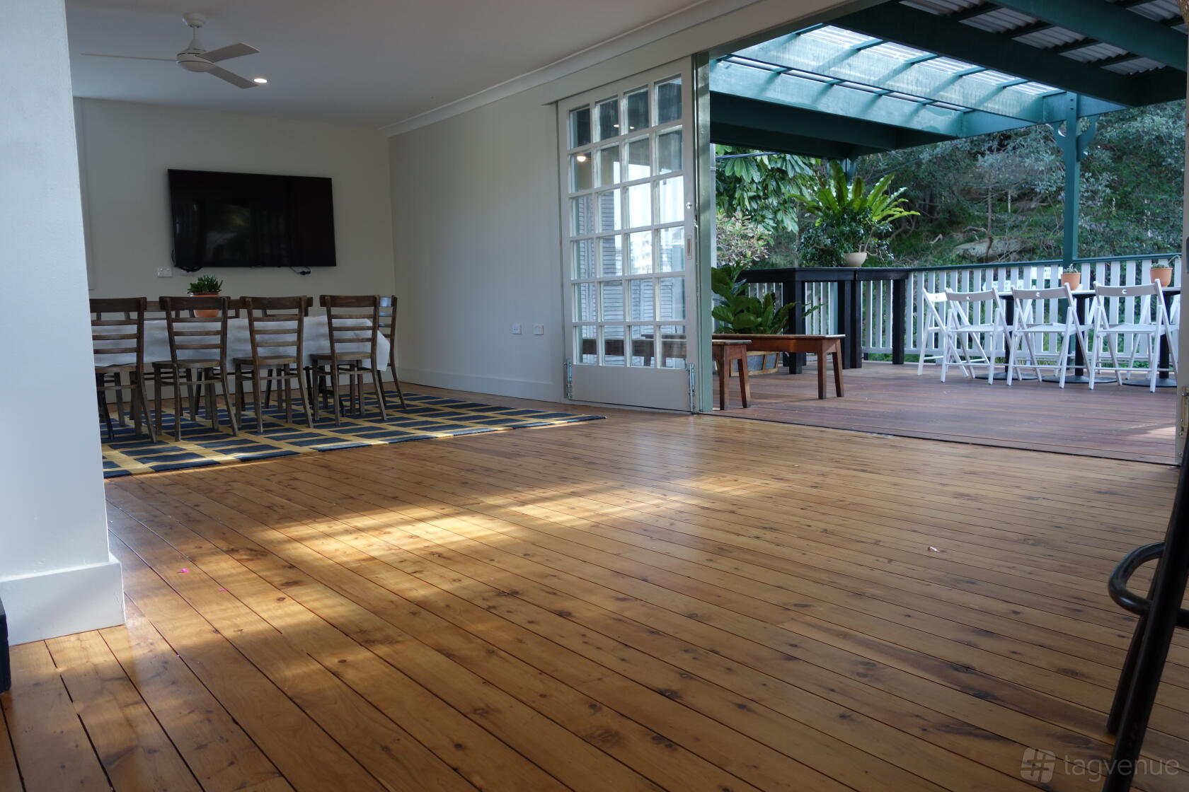 A bar with timber floors, long wooden tables, and glass doors opening to a covered deck at Mosman Rowers Club.