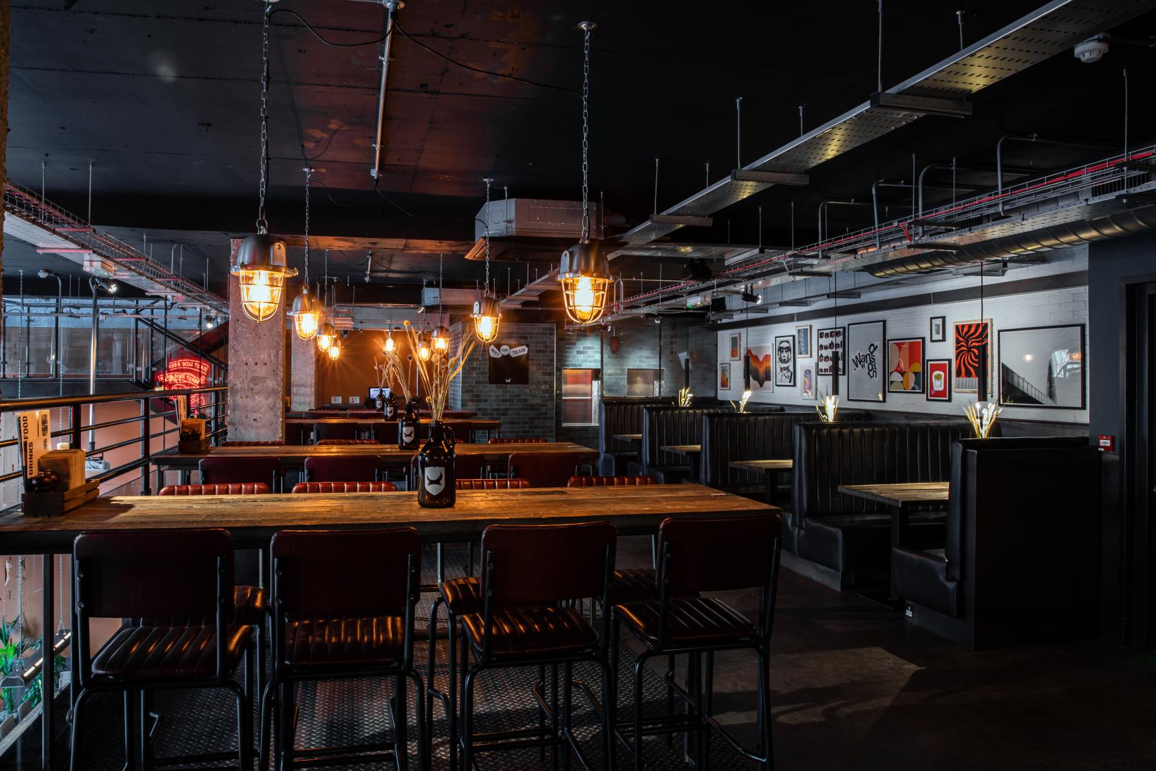 An event space in a bar with industrial lighting, exposed ceiling pipes, and booth seating at BrewDog Wandsworth.