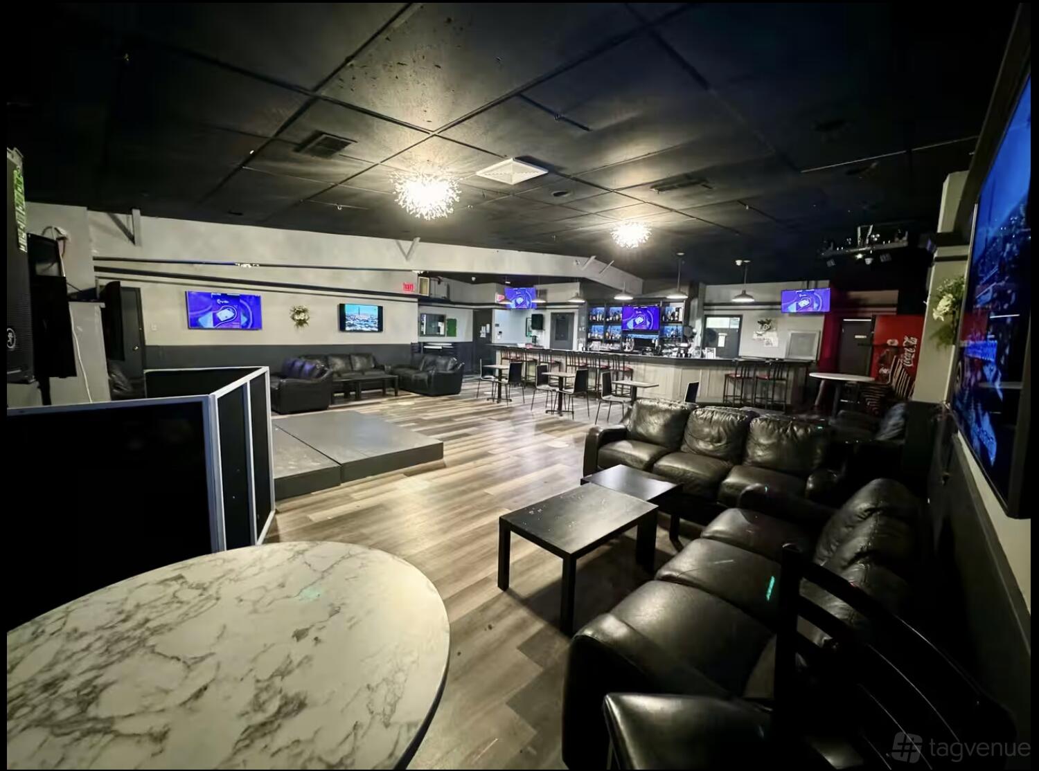 A bar with leather sofas, marble tables, wood flooring, and wall-mounted TVs at Elevate Lounge.