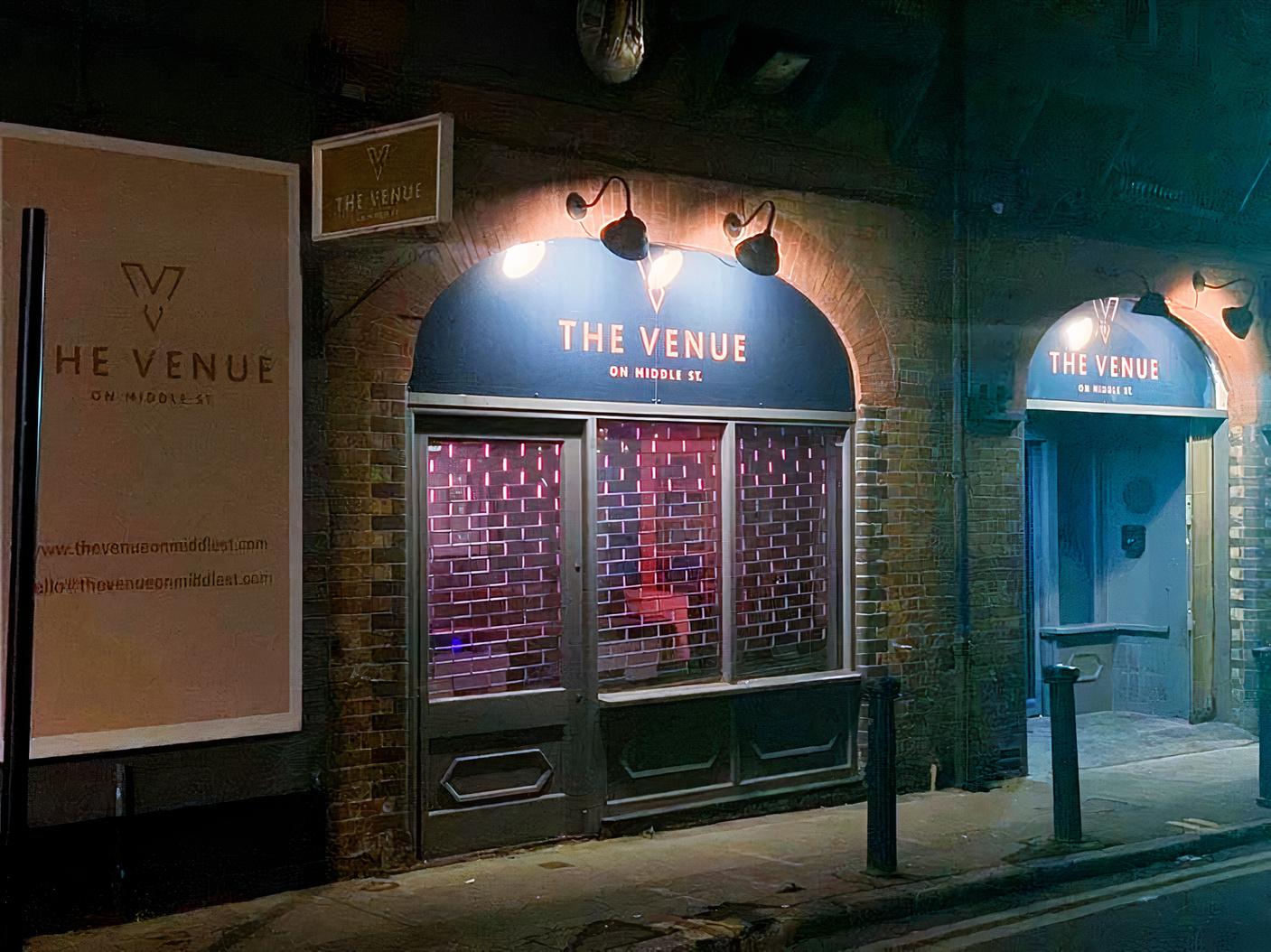 A brick building facade with arched windows and illuminated signage at The Event Rooms.