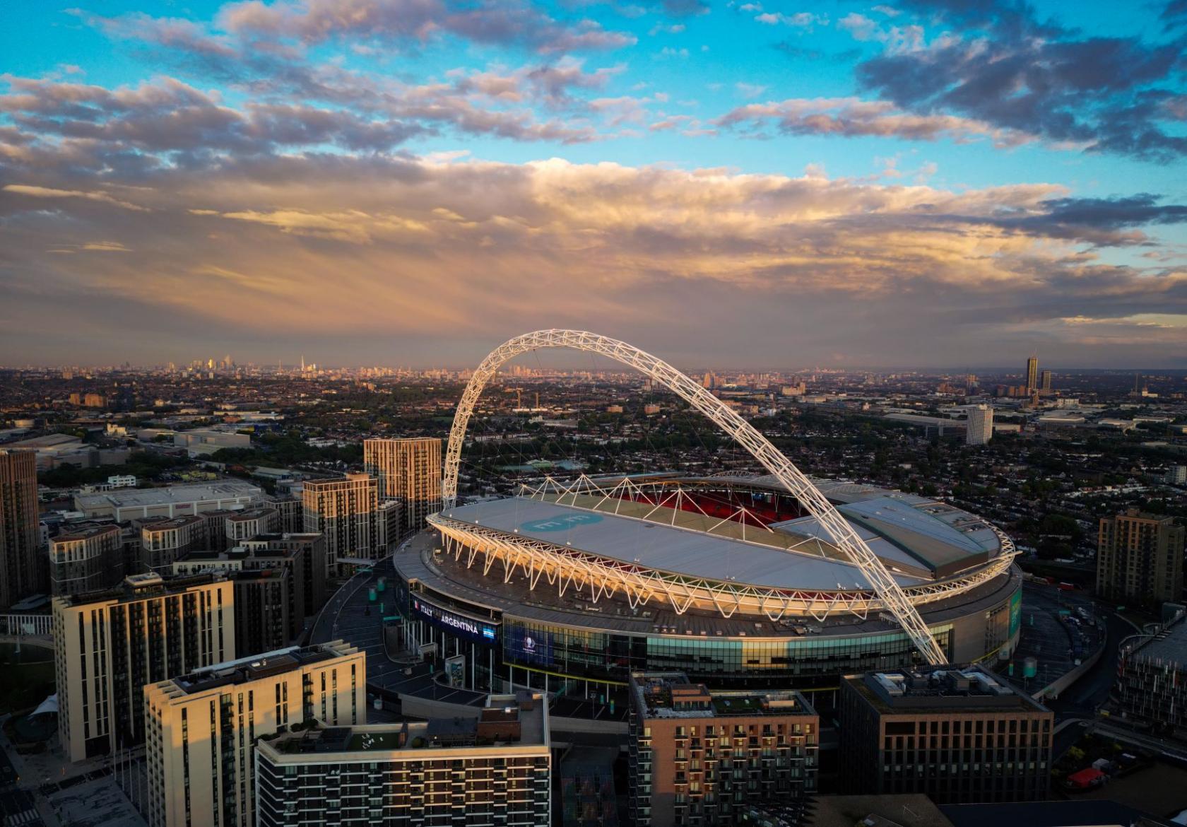 A stadium with a signature arch and circular seating bowl, surrounded by cityscape at Wembley Stadium.