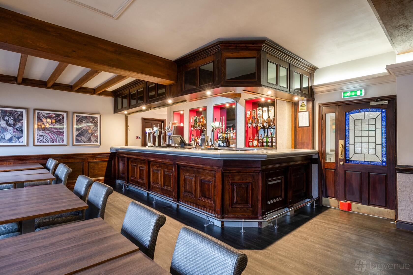 A hotel restaurant with a polished wooden bar, built-in shelving for drinks, and rows of tables at The Barn Hotel & Spa.
