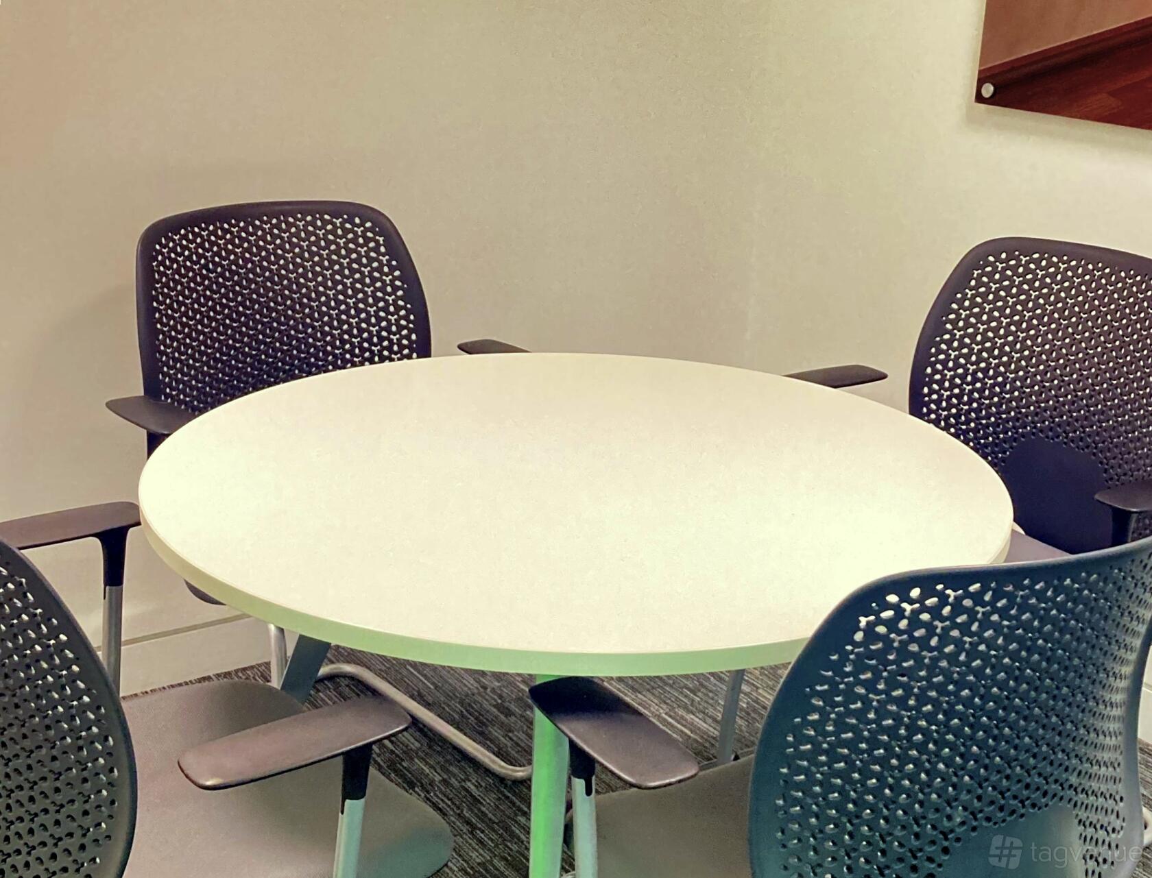 A meeting room with a round white table and four perforated black chairs at Rivvia Pronto Meeting Rooms.