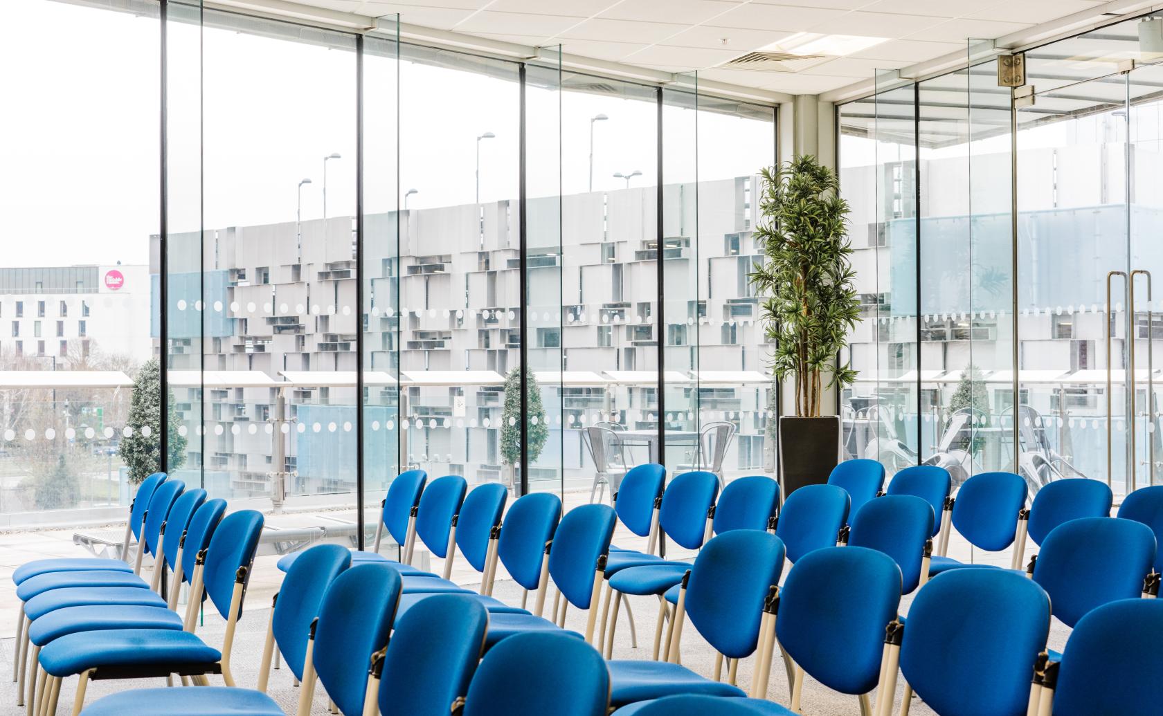 A conference centre with rows of blue chairs and floor-to-ceiling windows at Millennium Point.