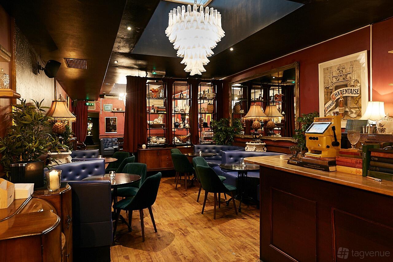 A cocktail bar with a chandelier, navy banquette seating, green velvet chairs, and mirrored back bar at Little Bat Bar & Kitchen.