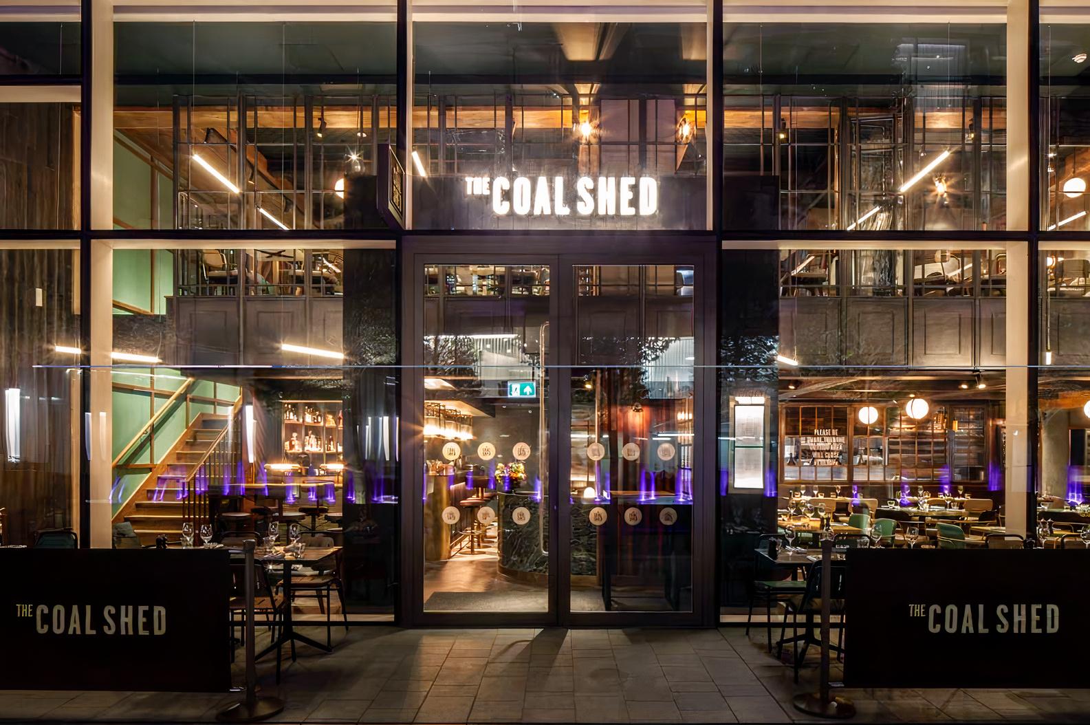 A restaurant with floor-to-ceiling windows, visible dining tables, and warm pendant lighting at The Coal Shed- London.