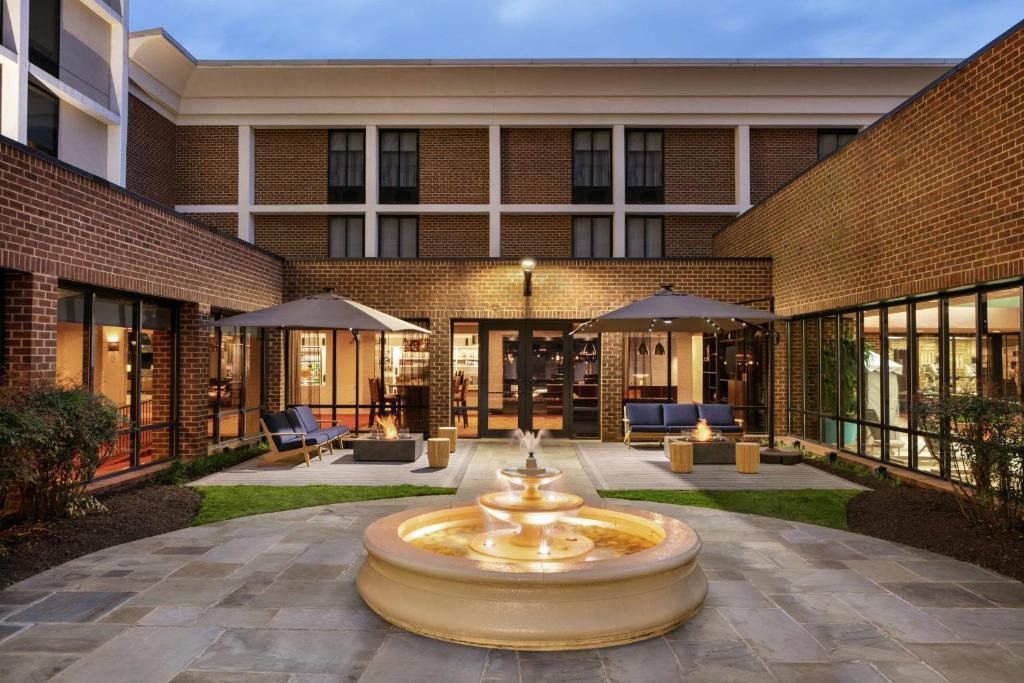 An outdoor restaurant patio with a central tiered fountain, lounge seating, and umbrella tables at Tyson's Social Tavern.