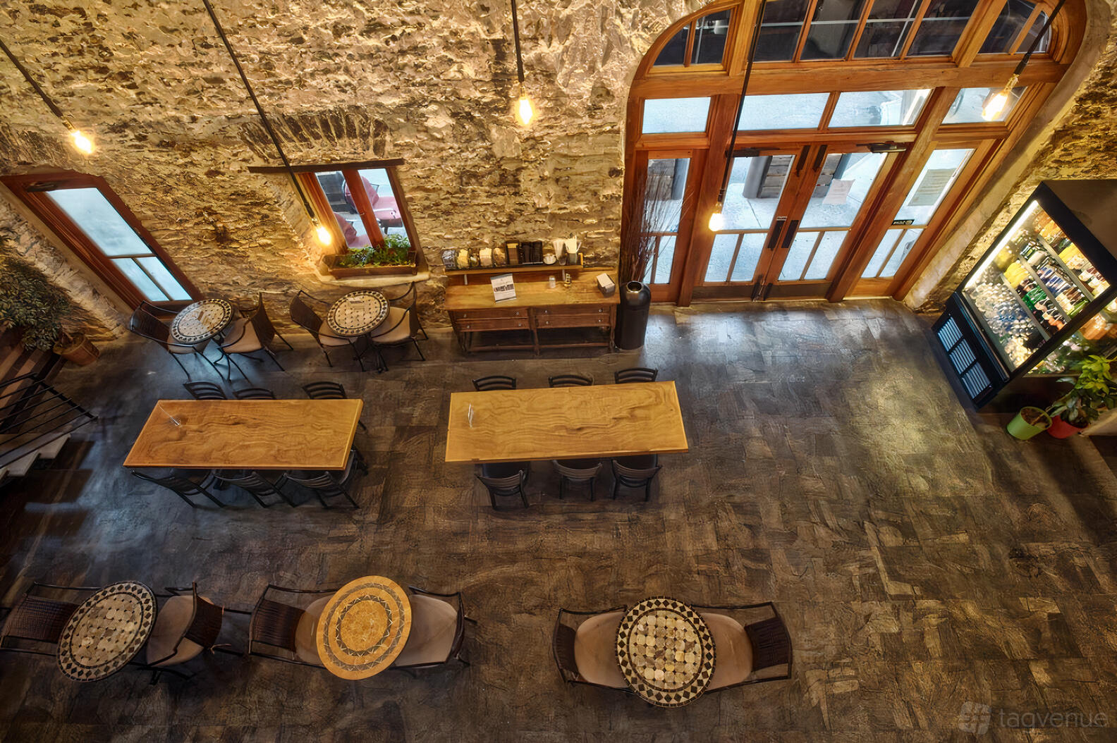 A restaurant with exposed stone walls, high ceilings, round mosaic tables, and large wood-frame windows at Founded Coffee & Pizza.