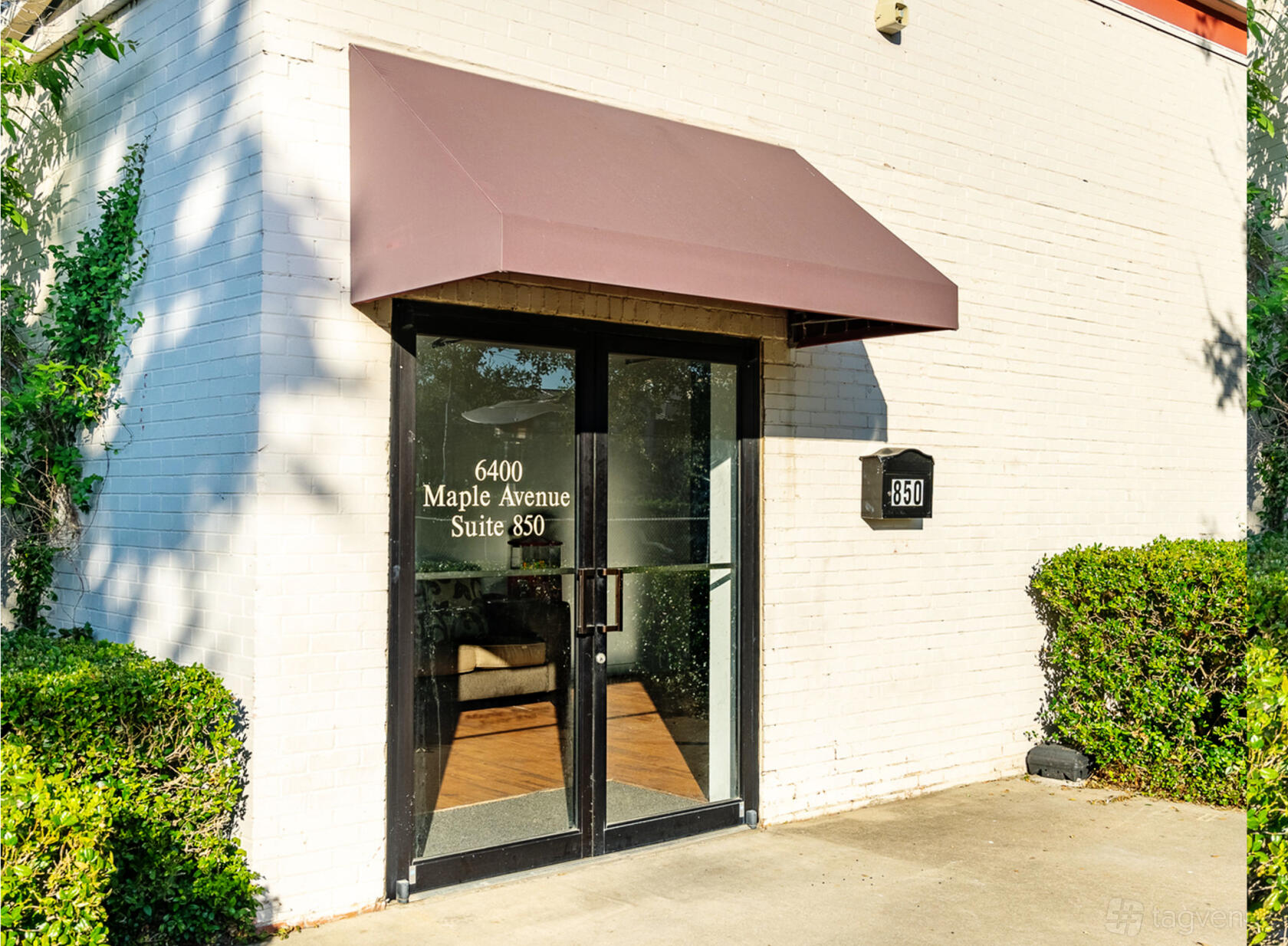 Entrance to a versatile event space with glass double doors, maroon awning, and greenery at L.A.Y.D Spaces @ Maple Ave.