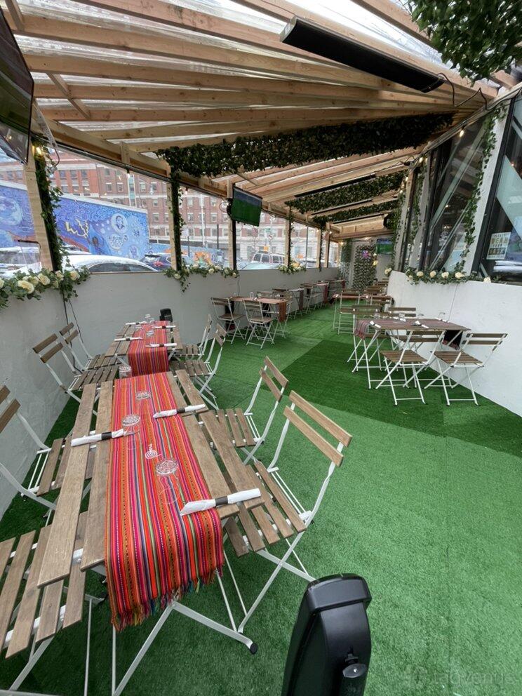 A restaurant with wooden tables, metal chairs, artificial grass flooring, and a glass roof at Pollo D' Oro.