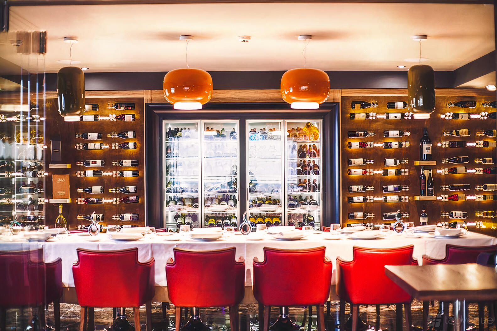 A dining room with red chairs, white tablecloths, and wall-mounted wine racks at Bella Cosa Restaurant.