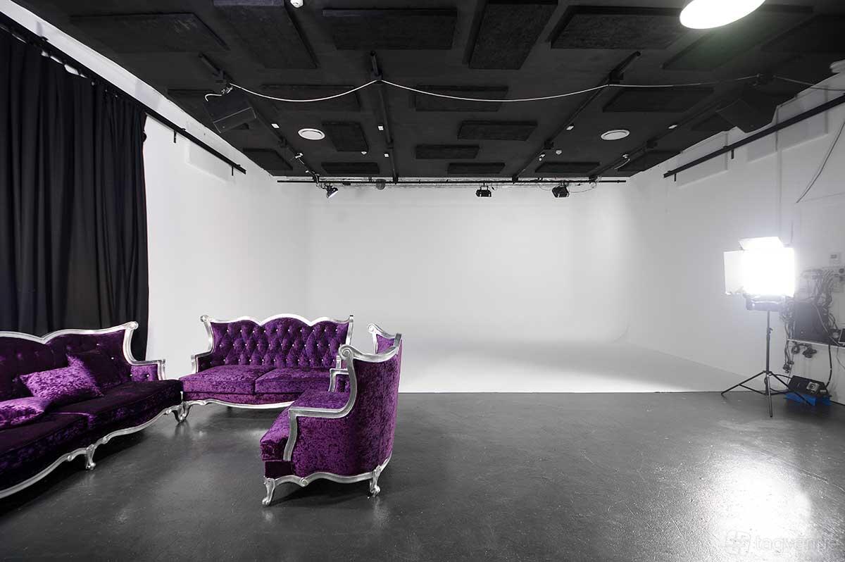 A photo studio with a white cyclorama wall, black ceiling panels, purple vintage sofas, and studio lighting at Sydney Props Photo Studios.