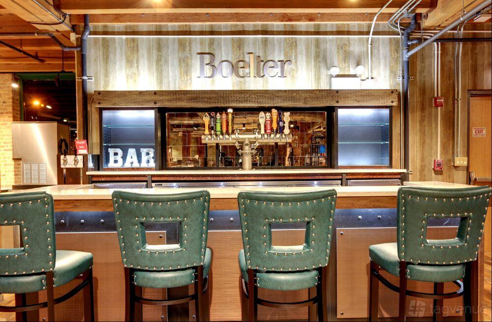 A bar in a restaurant with upholstered teal barstools, wooden walls, and a row of beer taps at Chicago Chefs' Table.