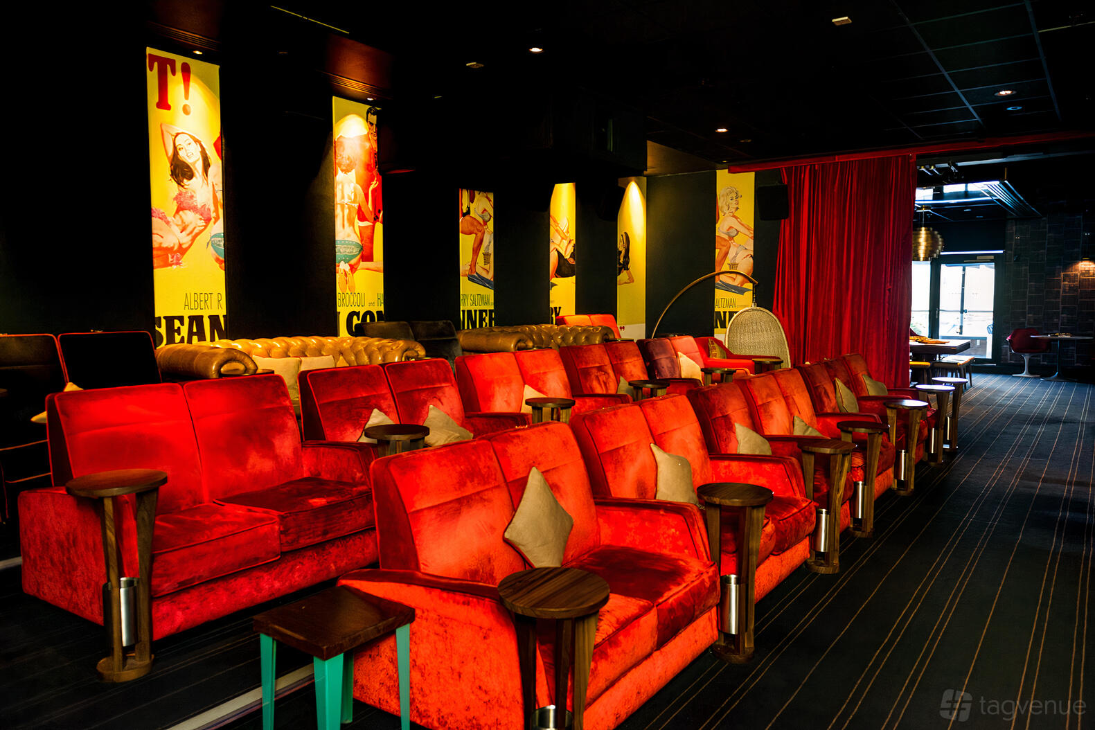 An auditorium with red velvet armchairs, small wooden side tables, and vintage film posters at Everyman Leeds.