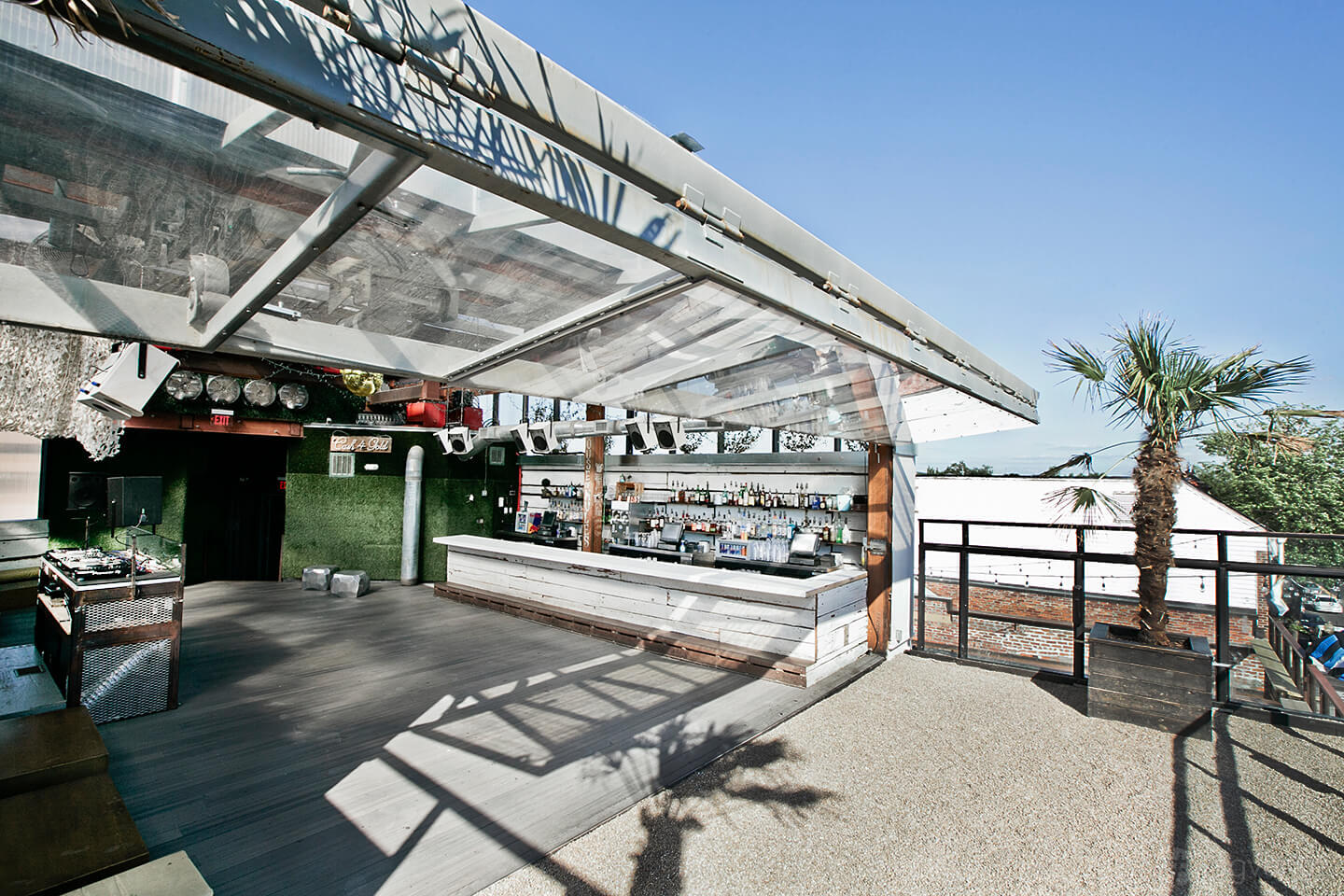 An open-air nightclub rooftop with a white bar, transparent awning, and potted palm trees at Flash.