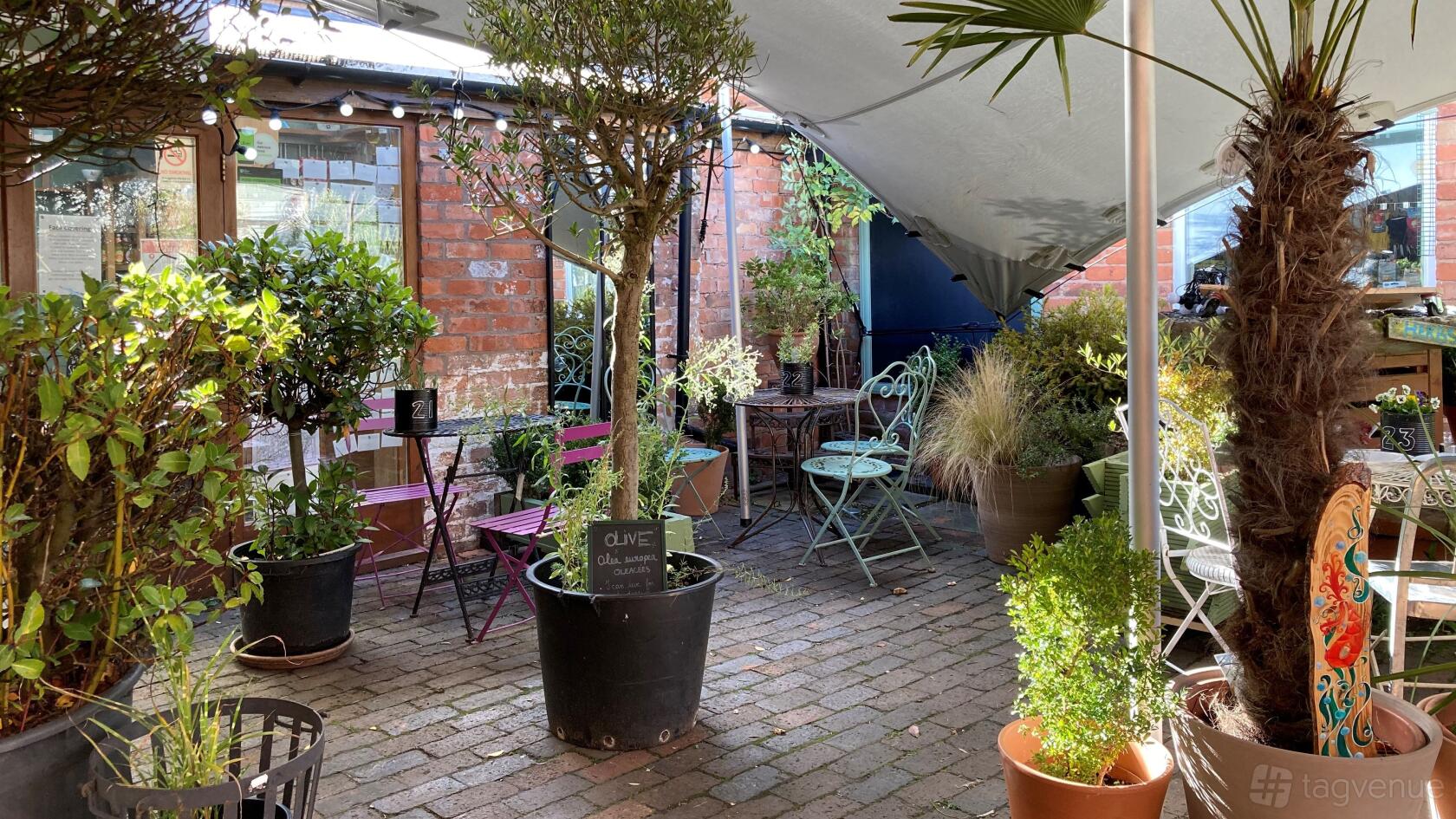 An outdoor cafe courtyard with brick flooring, lush potted plants, and metal bistro tables at Kitchen Garden Cafe.