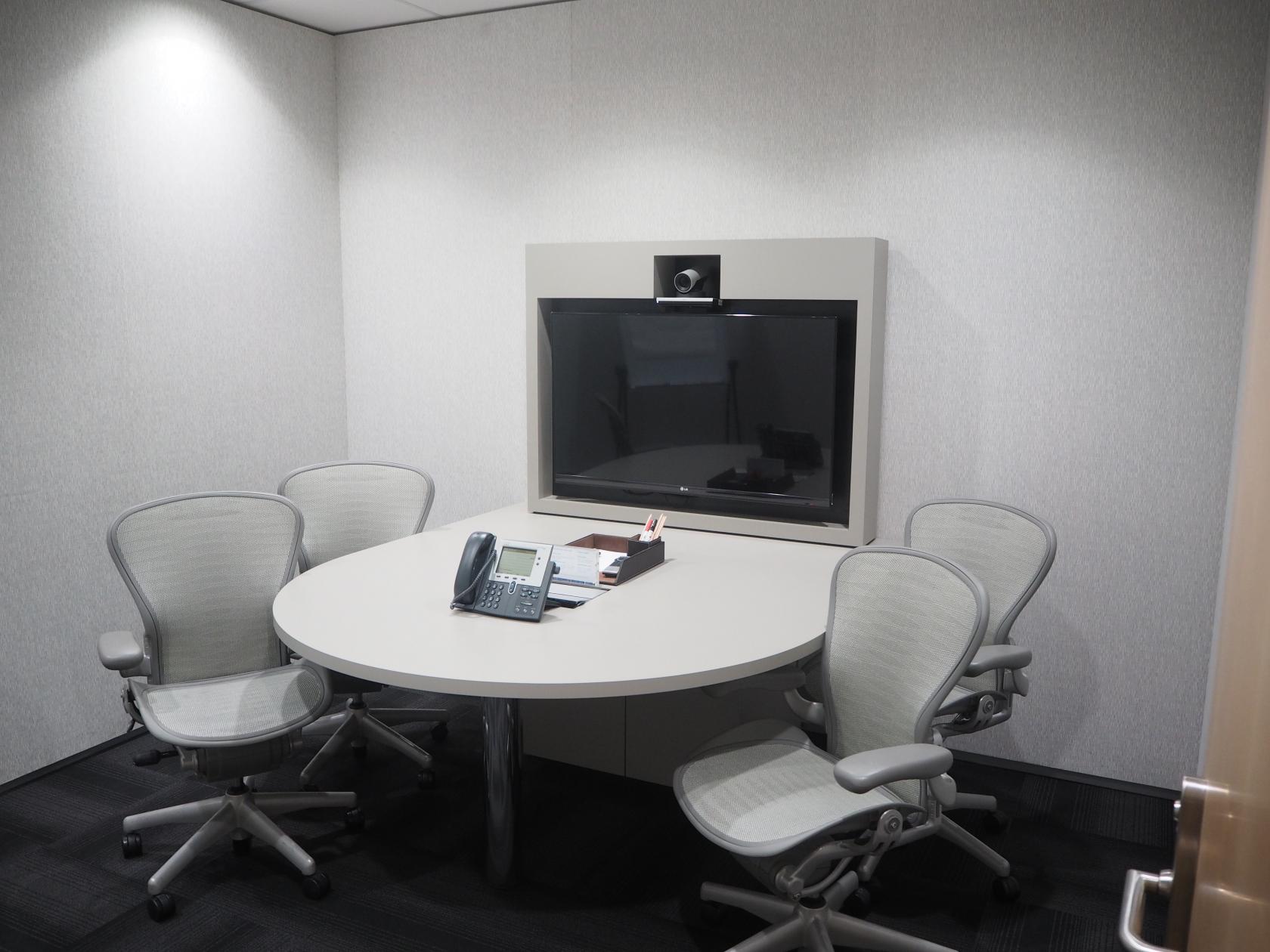 A meeting room with a round table, four ergonomic chairs, and a wall-mounted video conferencing screen at 108 St Georges Terrace.