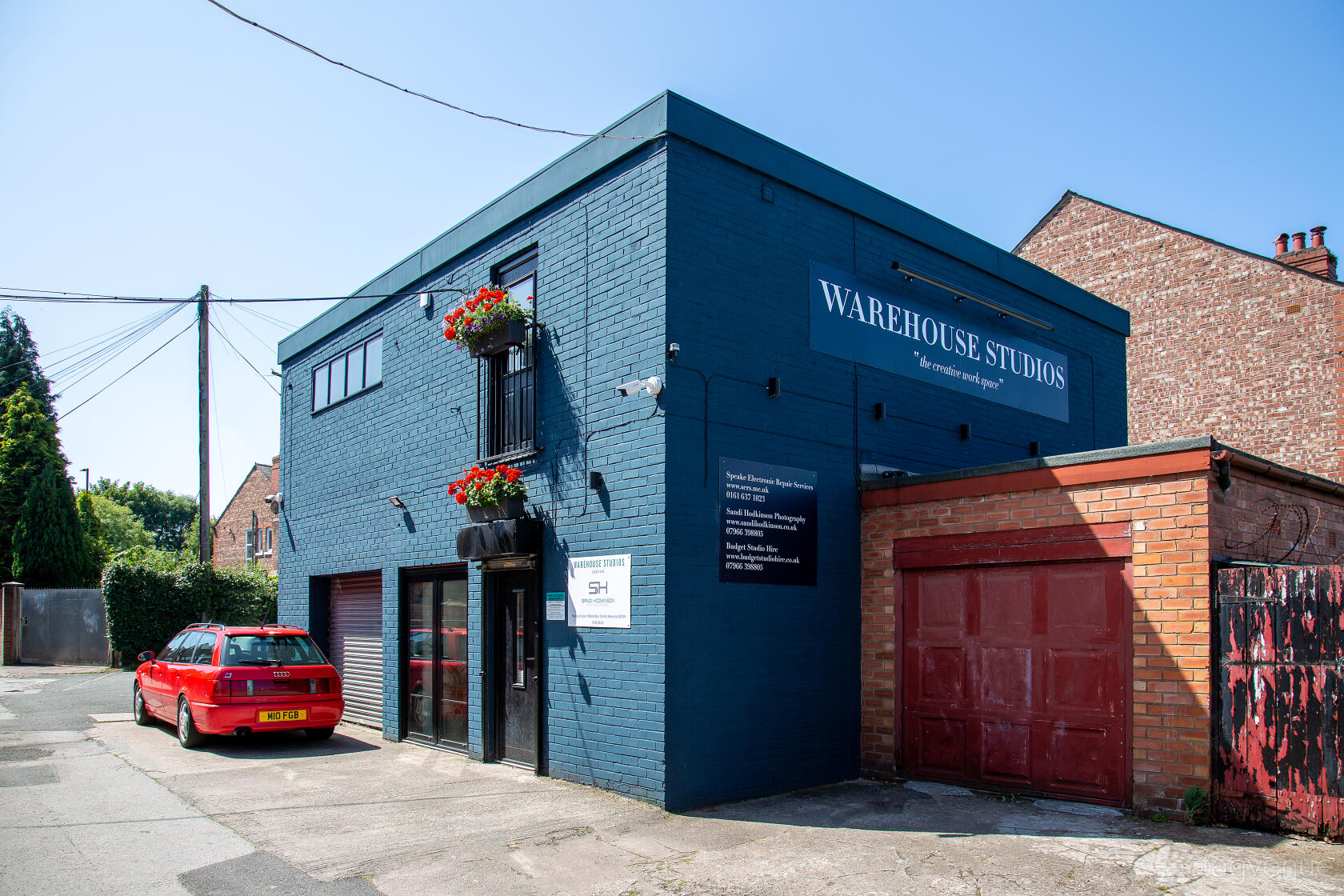 A film and photo studio with blue brick exterior, large windows, hanging flower baskets, and a garage at Budget Studio.