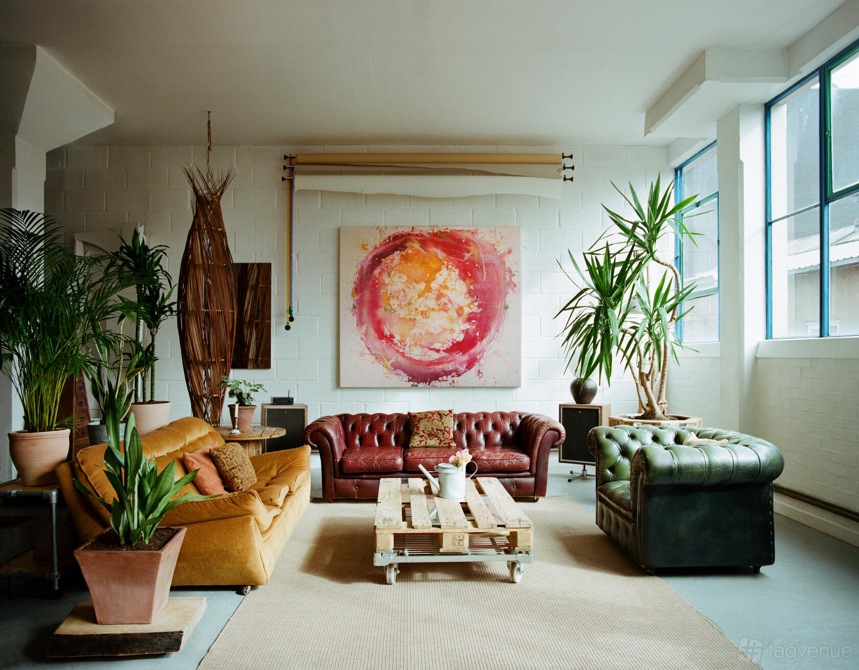 A loft with large windows, leather sofas, potted plants, and a colorful abstract painting at OSLO NINE.