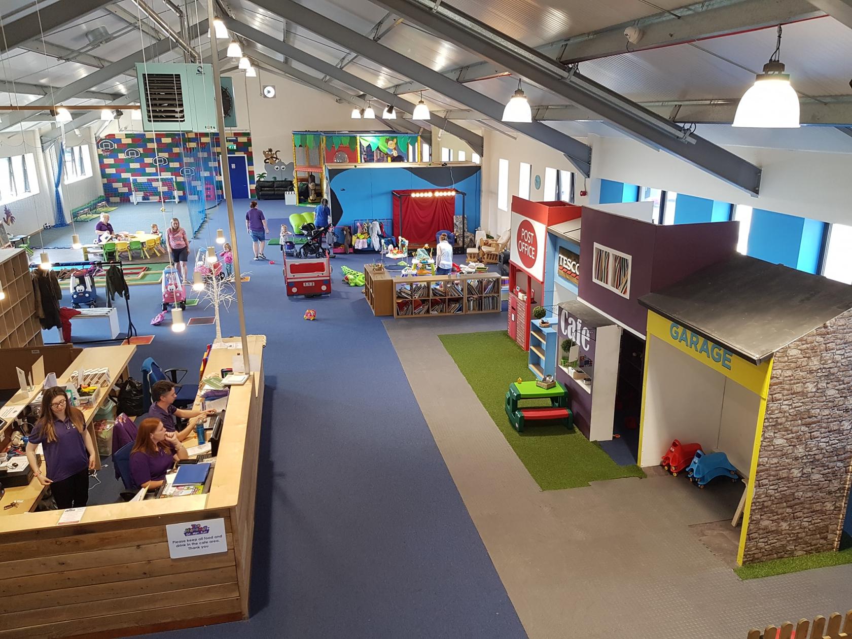 An event venue with colorful playhouses, a reception desk, and open play areas at The Hideaway Manchester.