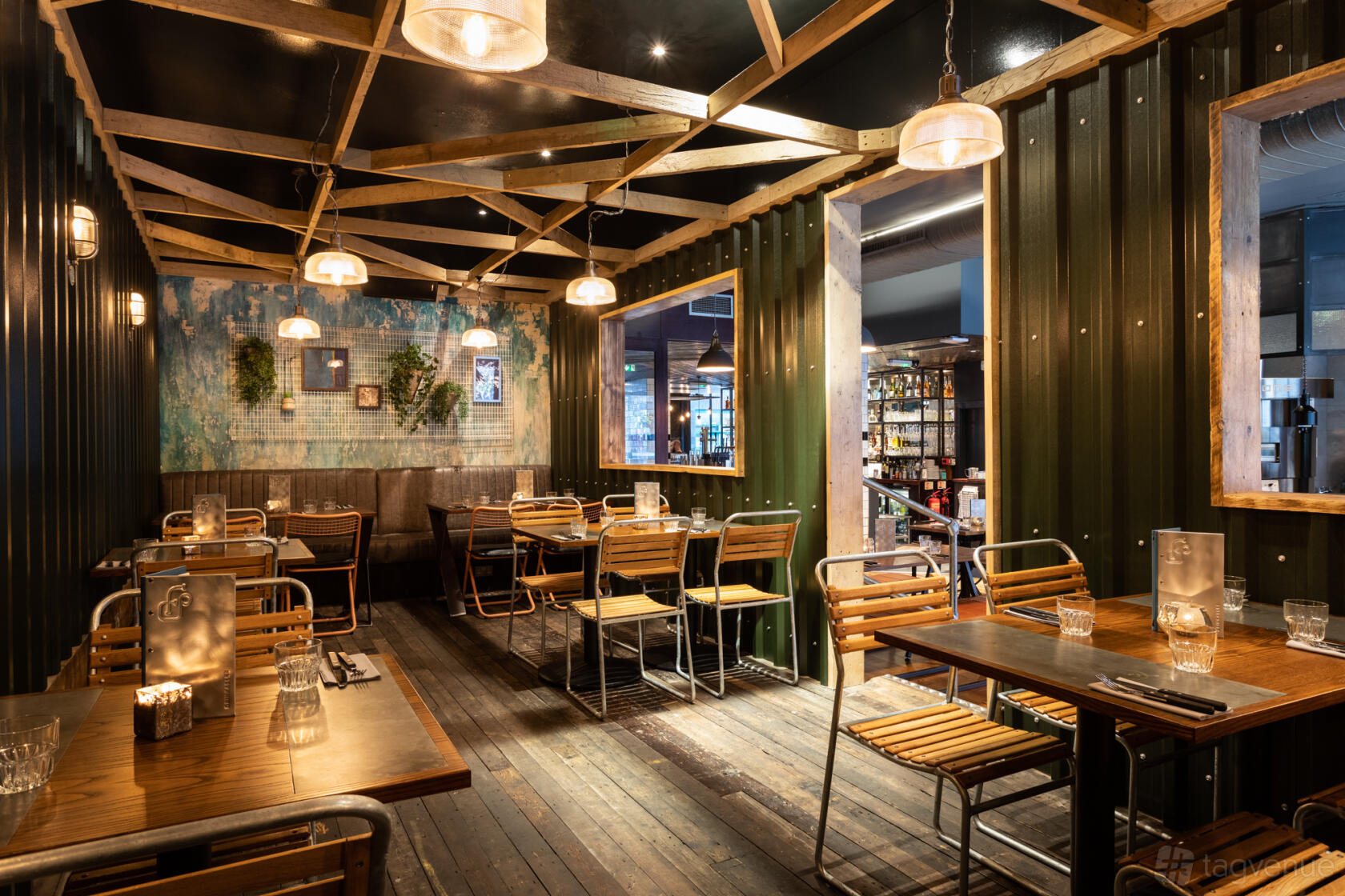 An event space in a bar with corrugated metal walls, wooden beams, and warm pendant lighting at Foundry Project.