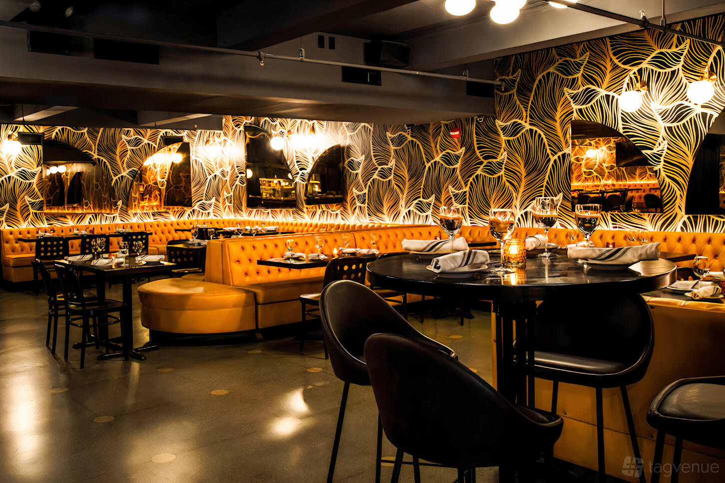 An event space in a bar with mustard yellow tufted banquettes, patterned wallpaper, and round tables at 5th and Mad.