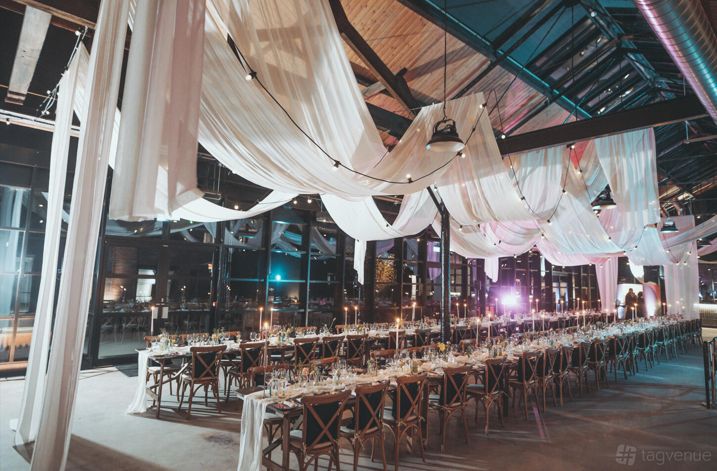 A historic building with draped fabric ceilings, string lights, and long banquet tables set for dinner at The Bond.
