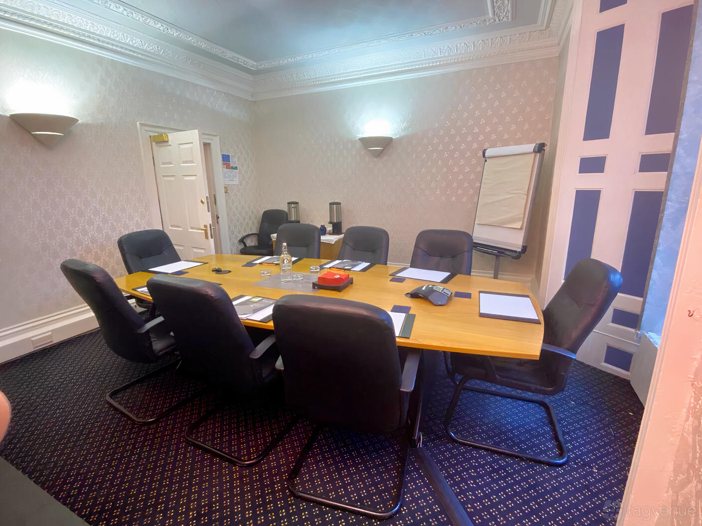 A meeting room with a wooden conference table, black chairs, wall sconces, and a flip chart at Leigh House - Leeds.