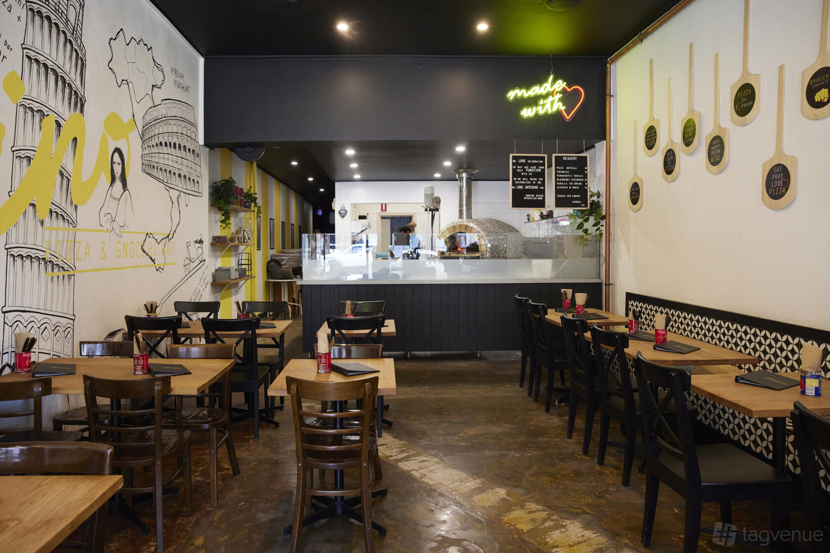 A restaurant with wood tables, wall murals, and a view of the open pizza oven at Piccolino Woodfired Pizza - Homemade Pasta.