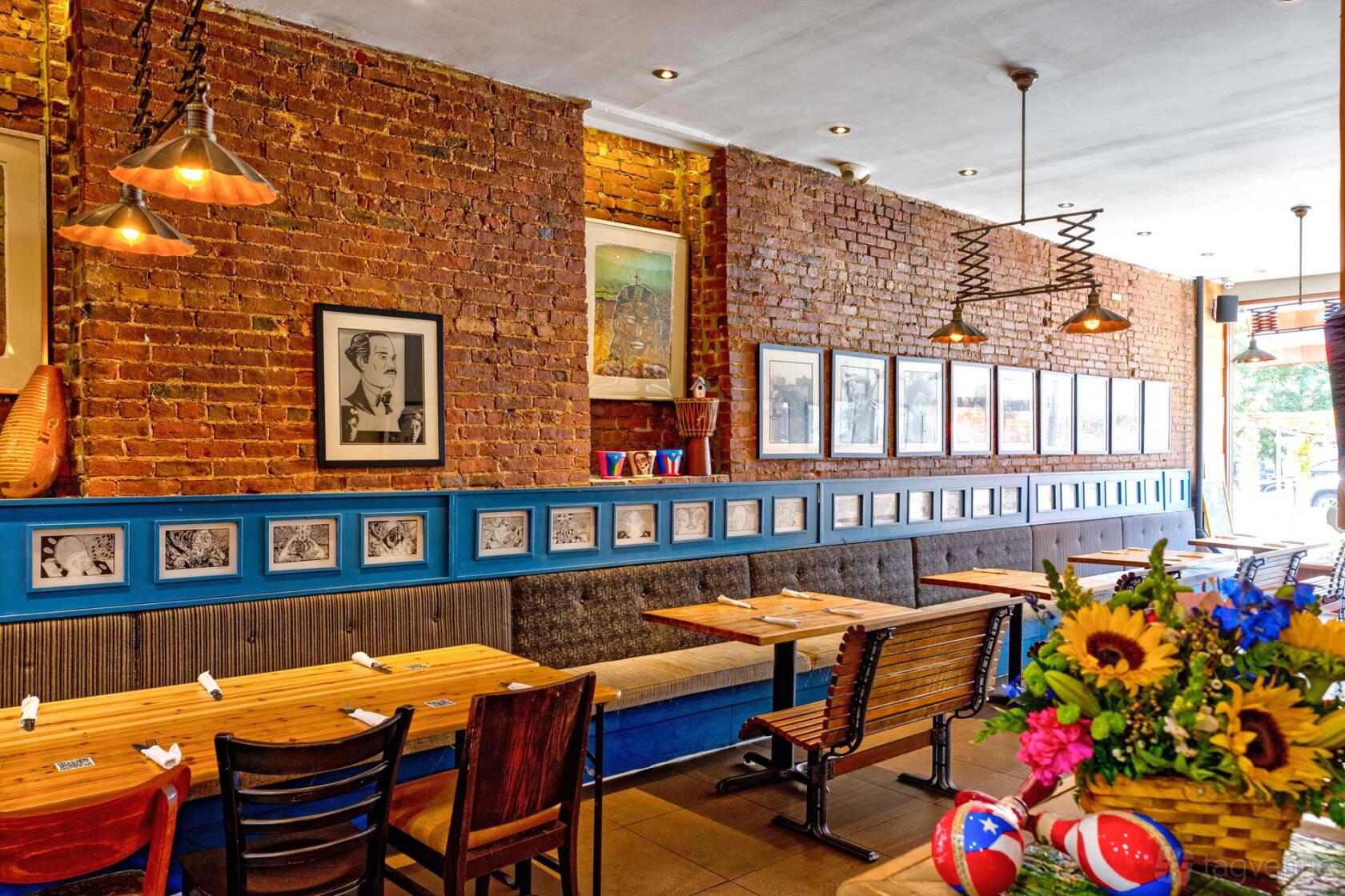 A restaurant with exposed brick walls, framed art, wooden tables, and a floral centerpiece at La Fonda.